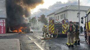 <p>Emergency services attend to a Glider bus, set on fire by protesters, on the Newtownards Road in east Belfast, as disorder flared on Tuesday. Picture: PA</p>
