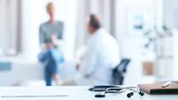 A male senior doctor consults with a female senior patient in a bright, modern office setting. The focus is on a stethoscope and