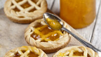Fresh baked tarts with marmalade filling and apricot jam in glass jar on cutting board on rustic wooden table.