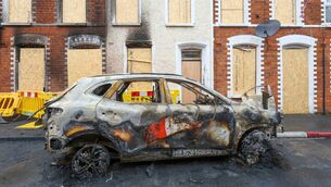 <p>The remains of a burnt-out car outside boarded-up houses off the Newtownards Rd, in east Belfast after two consecutive nights of violence following the June 8 stabbing of Stephen Ogilvie. Picture: Paul Faith/AFP/Getty </p>