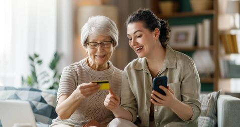 Happy Senior Woman Shopping Online With Daughter At Home Using Credit Card and Smartphone