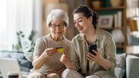 Happy Senior Woman Shopping Online With Daughter At Home Using Credit Card and Smartphone