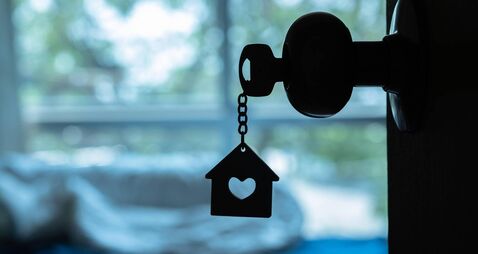 House key with home keyring in keyhole on wood door, copy space