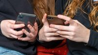 teenage school girls being cyber bullies  or just catching up on social media both on there phones, hand level  copy space above