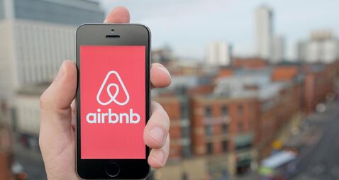 A man uses the Airbnb smartphone app while stood in a tall building overlooking a busy city street (Editorial use only)