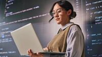 Young programmer analyzing code on laptop and large screen in modern office