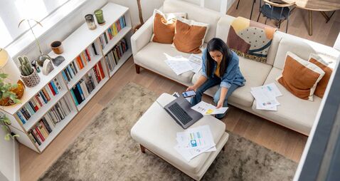 Woman working at home using her laptop and looking at documents
