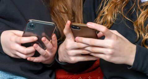 teenage school girls being cyber bullies  or just catching up on social media both on there phones, hand level  copy space above