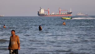 Residents swim in the waters of the Strait of Hormuz as a small motorboat passes cargo ships and other commercial vessels offshore near Bandar Abbas, Iran (Amirhosein Khorgooi/ISNA/AP)