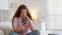 Emotional teenage girl using smartphone on bed at home, space for text