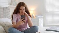Emotional teenage girl using smartphone on bed at home, space for text