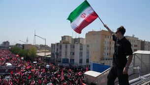 A man holds an Iranian flag as the truck carrying the coffin of the slain Iranian supreme leader Ayatollah Ali Khamenei and members of his family makes its way through mourners during the funeral procession in Tehran, Iran (Vahid Salemi/AP)