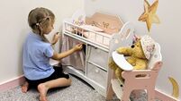 Girl playing with a toy crib and teddy bear in a nursery-themed play room
