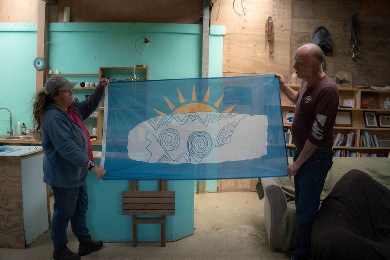 Fiona MacLachlan and Séamus Ó Drisceoil unfurl a flag featuring a neolithic inspited design