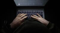 A simple, very dark night time image of hands on an illuminated keyboard typing. Shady person wearing a hood at a computer or la