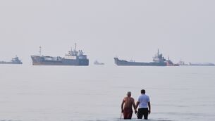 Two men wade in the waters of the Strait of Hormuz with vessels anchored in the background (Razieh Poudat/AP)