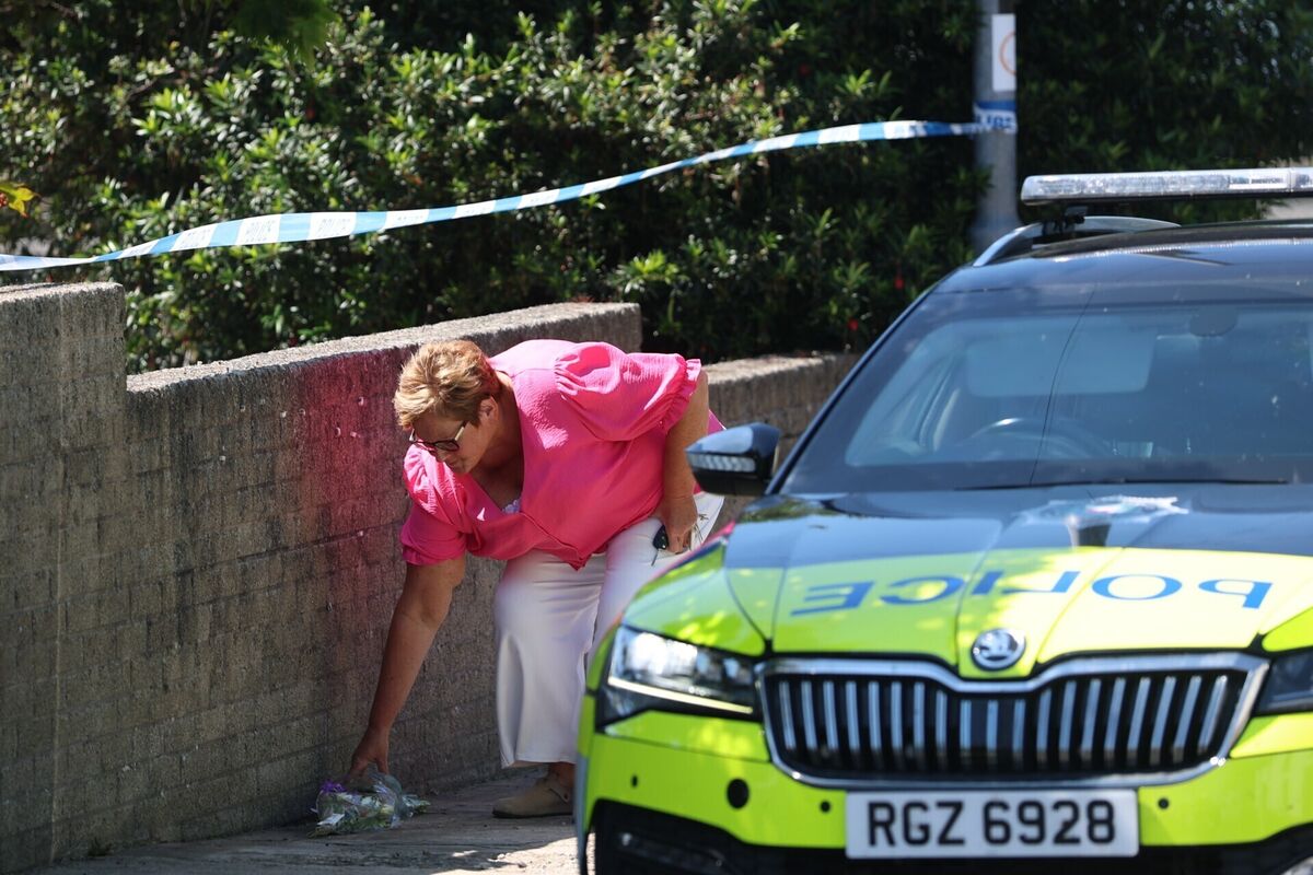 A woman lays flowers near the scene in the Old Cullybackey Road area of Ballymena, County Antrim, where three people were found dead inside a property on Monday morning. Picture: Liam McBurney/PA Wire A woman lays flowers near the scene in the Old Cullybackey Road area of Ballymena, County Antrim, where three people were found dead inside a property on Monday morning. Picture: Liam McBurney/PA Wire
