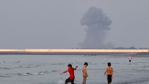 Three boys play in the shallow waters of the Strait of Hormuz, as a plume of smoke rises from an explosion in the background (Razieh Poudat/AP) Three boys play in the shallow waters of the Strait of Hormuz, as a plume of smoke rises from an explosion in the background (Razieh Poudat/AP)