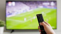 Close up of hand with black remote controller and tv with football on background