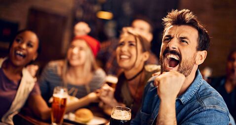 Sports fan and his friends watching a match on TV in a pub.
