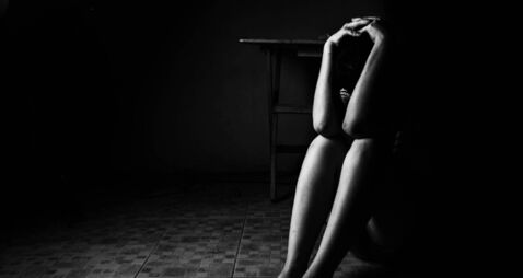 a woman sitting on ground with arm around lower head, sexual violence , sexual abuse, human trafficking concept