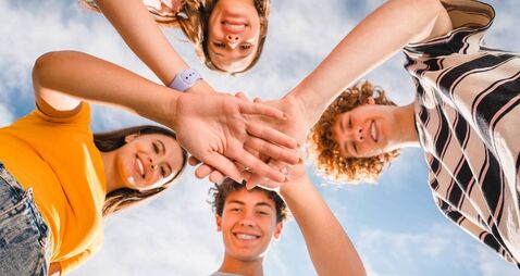 Low angle view of smiling boys and girls in casual giving high five stacking hands together outside