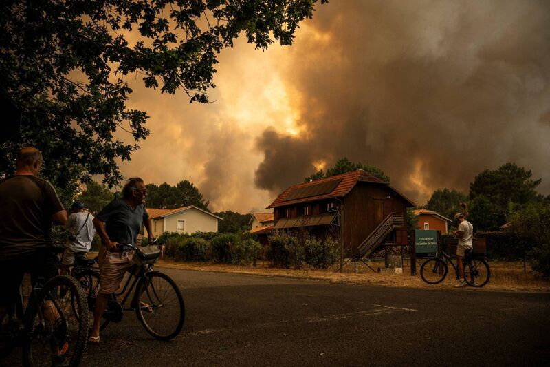 Residents on their bicycle look at smoke rising behind a residential area during a wildfire near Lege-Cap-Ferret, southwestern France on July 23, 2026. Picture: JULIEN DE ROSA / AFP via Getty Images
