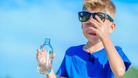 Portrait of a thirsty handsome boy in sunglasses drinking water on the desert tropical beach