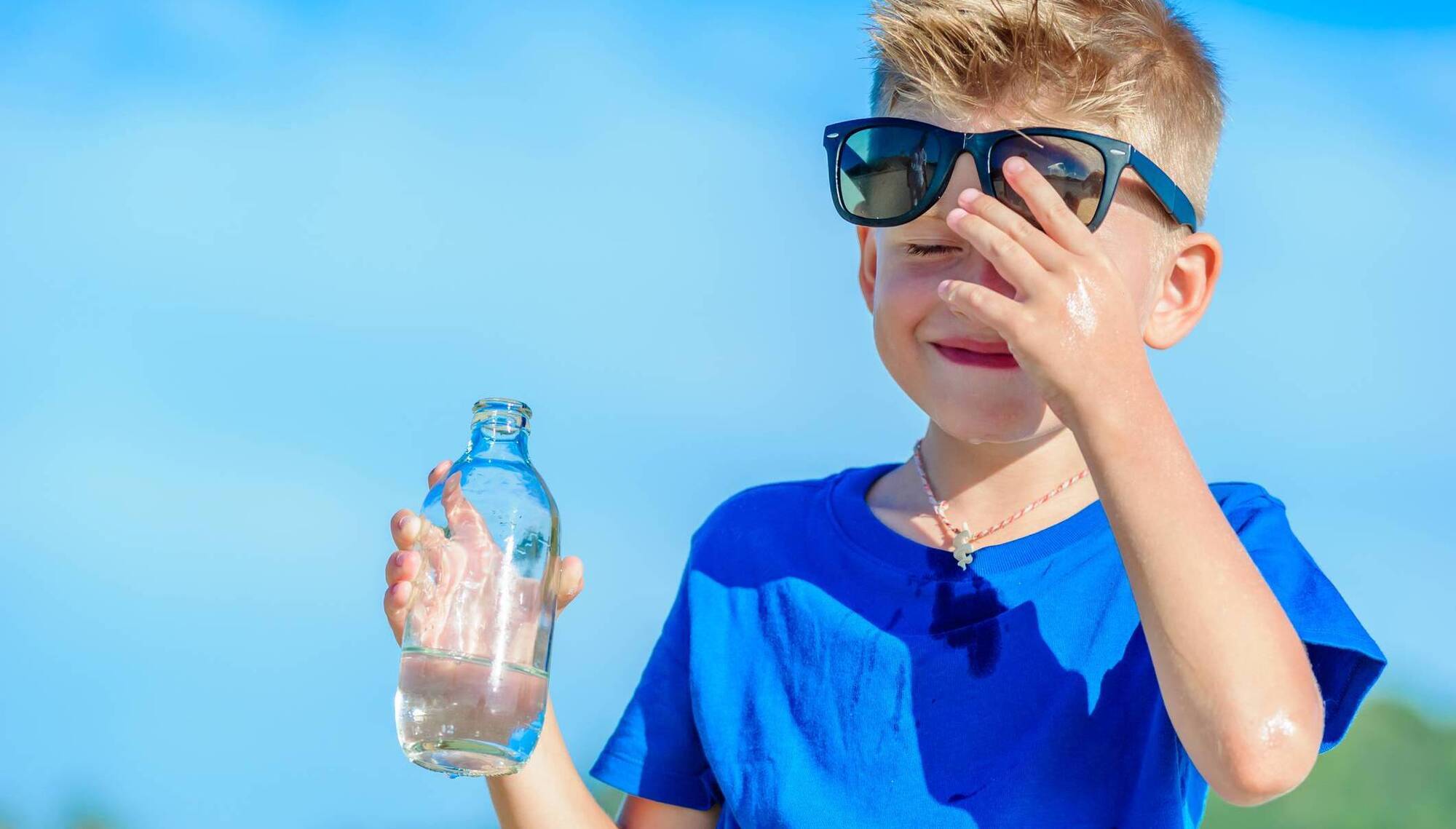 Portrait of a thirsty handsome boy in sunglasses drinking water on the desert tropical beach
