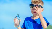 Portrait of a thirsty handsome boy in sunglasses drinking water on the desert tropical beach