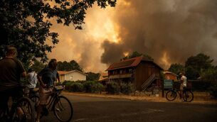 <p> Residents on their bicycle look at smoke rising behind a residential area during a wildfire near Lege-Cap-Ferret, southwestern France on July 23, 2026.  (Photo by JULIEN DE ROSA / AFP via Getty Images)</p>