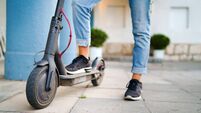 Close up on woman legs feet standing on the electric kick scooter on the pavement wearing jeans and sneakers in summer day