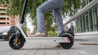 Feet of unknown woman standing by or driving electric kick scooter e-scooter on the pavement in day eco friendly modern transpor