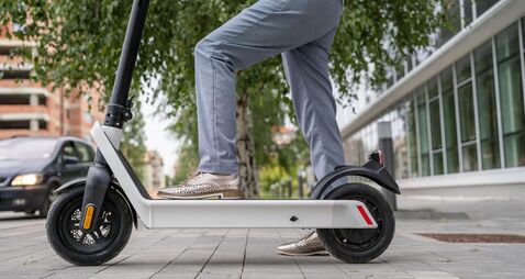 Feet of unknown woman standing by or driving electric kick scooter e-scooter on the pavement in day eco friendly modern transpor