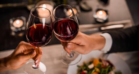 Close up of young couple toasting with glasses of red wine at restaurant