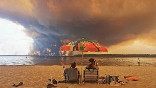 <p> Beach goers rest on the beach of Moutchic on the shore of Lake Lacanau (Etang de Lacanau) in Lacanau , southwestern France on July 24, 2026, as clouds of smoke rise into the sky from the Gironde wildfire. (Photo by Maximilien LAMY / AFP via Getty Images)</p>