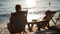 Young couple sitting on lounge chairs and relaxing on the beach while enjoying view of setting sun reflecting on calm sea water