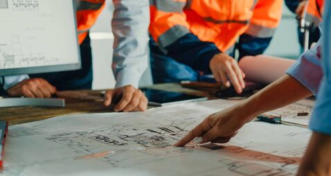 Closeup of team of industrial engineers meeting analyze machinery blueprints consult project on table in manufacturing factory.