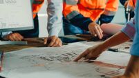 Closeup of team of industrial engineers meeting analyze machinery blueprints consult project on table in manufacturing factory.
