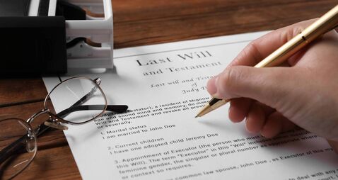 Woman signing Last Will and Testament at wooden table, closeup