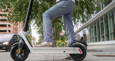 Feet of unknown woman standing by or driving electric kick scooter e-scooter on the pavement in day eco friendly modern transpor