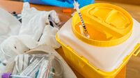 Hand with blue latex glove throws syringe into yellow waste container in hospital