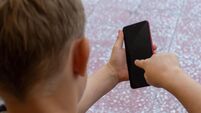 Young boy sitting outside holding a mobile or cellular smart phone. Connectivity, internet, millenial, screen time concepts.