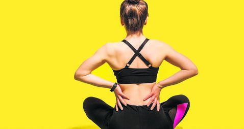 Back view, sportswoman sitting on mat and touching sore spine, suffering backache after physical training