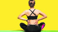 Back view, sportswoman sitting on mat and touching sore spine, suffering backache after physical training