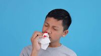 Young Boy Experiencing Nosebleed, Seeking Help with Tissue to Stop the Flow on Blue Background