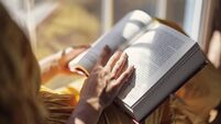 Teenage girl sitting on windowsill and reading a book