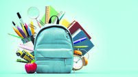 Blue backpack with alarm clock and school equipment. Back to school concept on blue background with copy space.