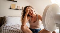 Overheated woman trying to cool down with fan at home