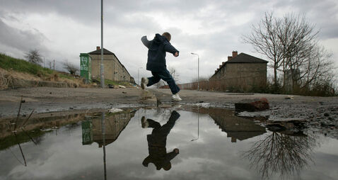 B5C161 a child leaps over a puddle on a poverty stricken estate in Maryhill Glasgow